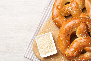 Delicious pretzels and bowl with sesame seeds on white wooden table, flat lay. Space for text
