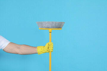 Man with yellow broom on light blue background, closeup