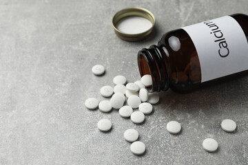 Overturned bottle of calcium supplement pills on grey table. Space for text