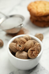 Nutmeg seeds in bowl on white marble table, closeup