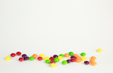 Multicolored round candies scattered on a white table with copy space. Beautiful sweets.