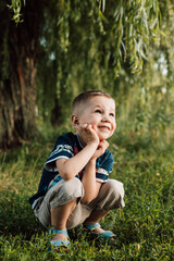 A little boy crouched under a tree, his hand propping up his head and smiling