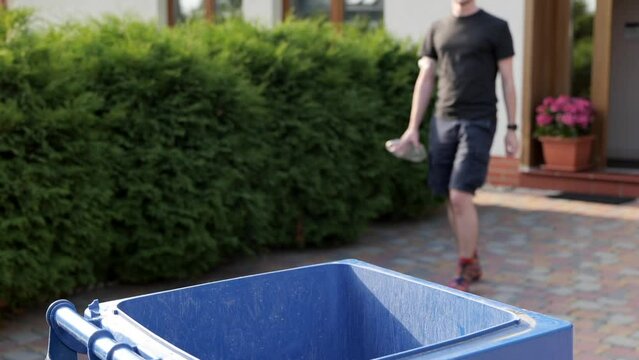 Unrecognizable man  walks out to throw plastic bottles into trash bin in garden