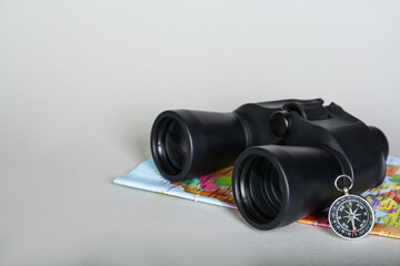 Modern binoculars, compass and map on grey background, space for text