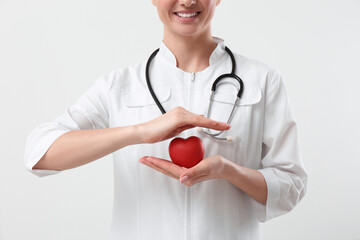 Doctor with stethoscope and red heart on white background, closeup. Cardiology concept