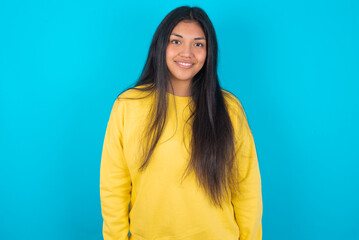 Fototapeta premium young latin woman wearing yellow sweater over blue background with nice beaming smile pleased expression. Positive emotions concept