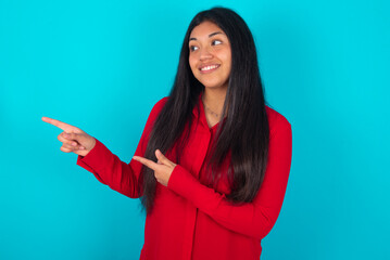 Optimistic young latin woman wearing red shirt over blue background points with both hands and ...
