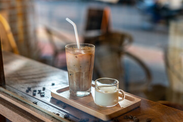 A tall glass of iced latte coffee with milk cream on a wooden counter bar over a cafe glass window...