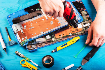 Wizard repairs laptop with tools and hands on the blue wooding table. top view