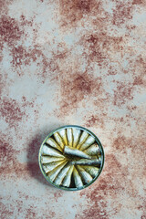 Overhead view of a large round sardine tin on a weathered and painted textured background. Food storage and fish.