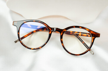 Leopard glasses on white silk fabric, close-up. Stylish women's glasses in a leopard-colored frame