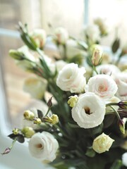 Obraz na płótnie Canvas Beautiful spring delicate bouquet of white flowers of lisianthus, eustoma on the window close-up. Mother's day card. Wedding concept. Floristry, floral studio