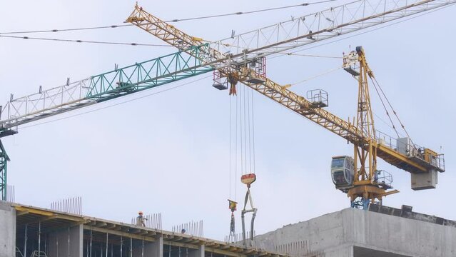 Builders gesturing talking in slow motion standing on unfinished skyscraper with tower cranes. Professional Caucasian men building real estate house outdoors in Kyiv, Ukraine
