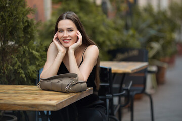 young smiling woman is sitting at the table outdoors. City Style