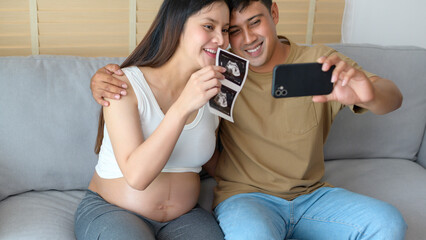 Young pregnant woman with husband embracing and video call with family and friends by smartphone on social media, family and pregnancy care concept