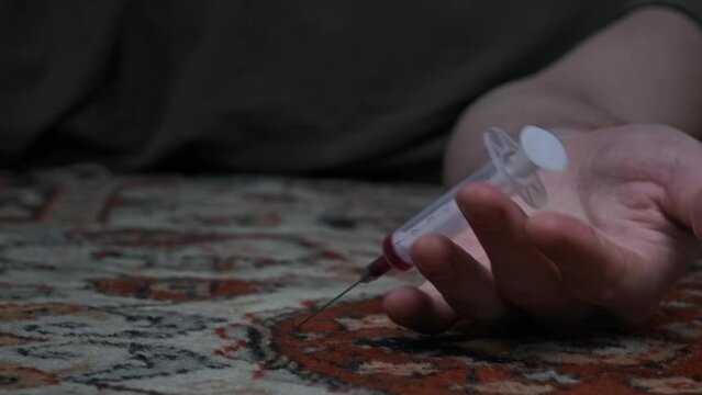 Addict's hand with syringe falls to floor just pricked heroin drugs. Slow Motion. Overdose, meth syringe falls out of weakened hand of die junkie. Social degradation, self-destruction, narcomaniac. 4K