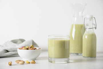 Pistachio milk in glasses and pistachios in glass jar on white kitchen background. Vegan nutty plant based milk. Vertical.