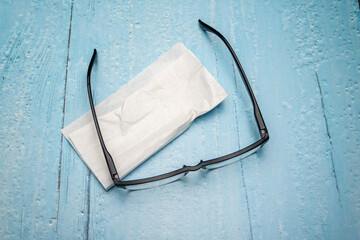 Top view of reading glasses with black temples and glasses cleaning cloth on light blue lacquered...