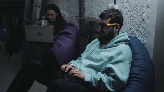 Handheld shot of a man and a woman programming and hiding in the basement during the war because of the danger of a bomb attack