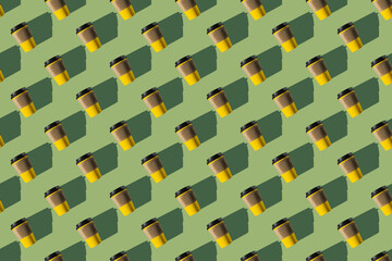 Pattern of yellow paper coffee cups on a green background. Flat lay