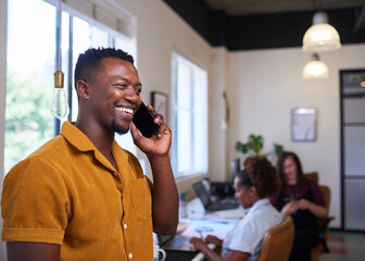 A creative businessman takes a call in the office with colleagues in background