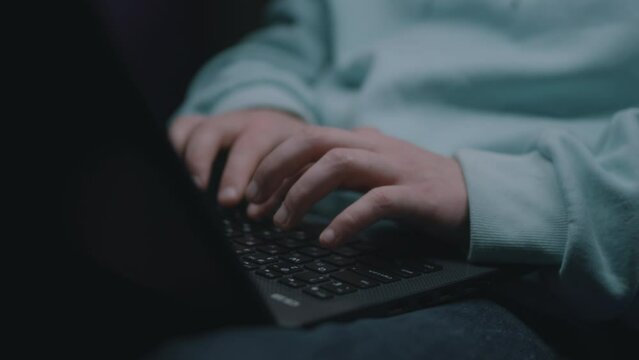 Crop view of web developer hands sitting in a dark bomb shelter, during the war typing code on the keyboard and creating a website on a laptop