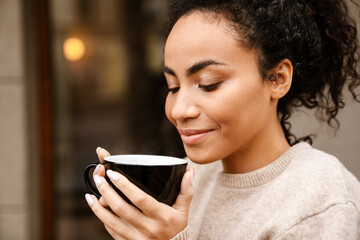 Young black woman smiling and drinking coffee outdoors