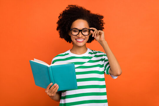 Portrait of attractive cheerful intellectual wavy-haired girl reading diary touching specs isolated on bright orange color background