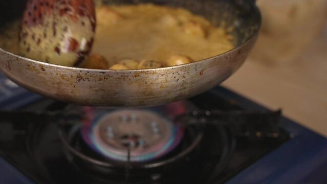 Professional chef using wooden mixing spoon stirring the delicious coconut yellow curry seafood scallops and swirling the frying pan at the same time.