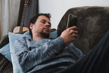 Young Caucasian male is lazy on a couch looking at his phone