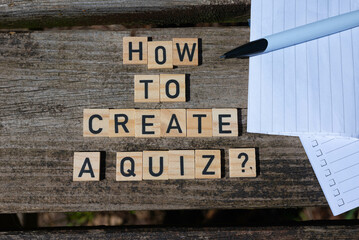 How to create a quiz? Black capital letter words on wooden toy blocks on a natural garden table background with paper and pen.