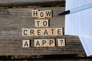 Wooden toy blocks with the text how to create a app with pen and paper in the background