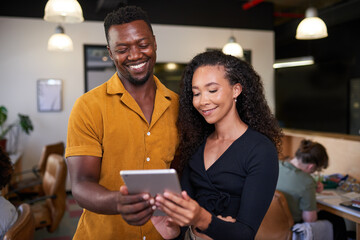Fototapeta premium Two creative colleagues look at a digital tablet in an open plan office