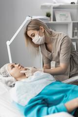 cosmetologist doctor makes an injection of hyaluronic acid in the lips of a client