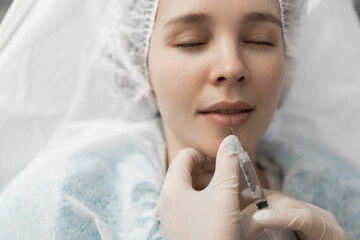 a cosmetologist doctor makes an injection of hyaluronic acid into the lips of a client. Lip...