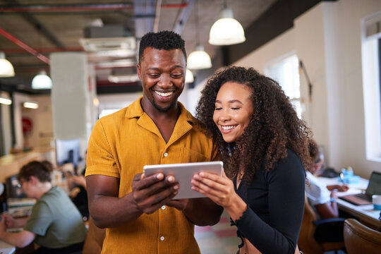 Two creative colleagues look at a digital tablet in an open plan office