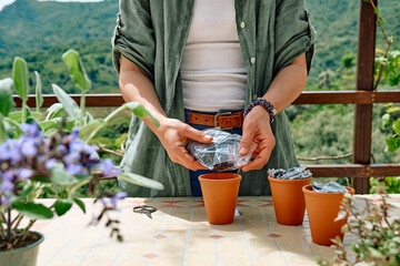 Woman sowing medicinal or aromatic herbs in clay pot on balcony. Home planting and food growing. Sustainable lifestyle. Taking care of plants, growing herbs and flowers in small garden in apartment.