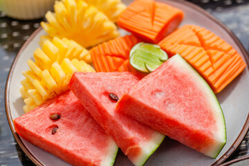 Plate with cutting ripe fresh exotic tropical fruits - pineapple, papaya with lime and watermelon. Vegan breakfast in hotel. Assorted of juicy healthy raw sweet food.