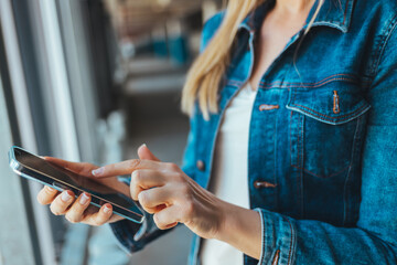 Obraz premium A clip shot of a beautiful young woman using a smartphone. The woman uses a smartphone in the parking lot, exchanges messages or browses social networks.