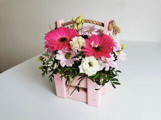 Beautiful pink flower box with gerberas, eustoma, chrysanthemums, pistachios, gypsophila on a white table. Minimalist arrangement with flowers.