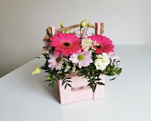 Beautiful pink flower box with gerberas, eustoma, chrysanthemums, pistachios, gypsophila on a white table. Minimalist arrangement with flowers.
