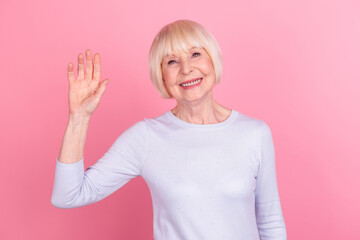 Photo of cheerful mature woman good mood waving hand hello meet friends isolated over pink color background