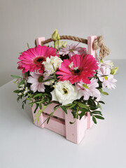 Beautiful pink flower box with gerberas, eustoma, chrysanthemums, pistachios, gypsophila on a white table. Minimalist arrangement with flowers.