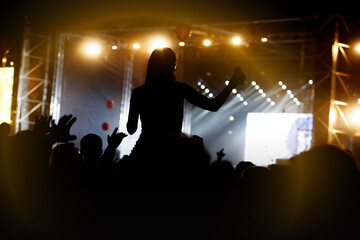 Girl silhouette with raising hands and mobile phone during enjoying music concert.