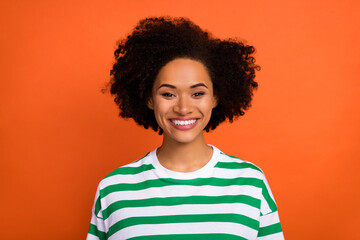Portrait of attractive toothy cheerful girl wearing striped tshirt isolated over bright orange...