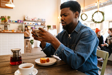 Fototapeta na wymiar Black smiling man using mobile phone while having brunch in cafe