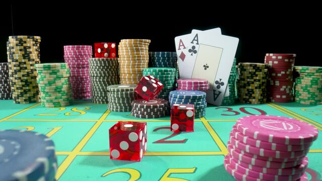 Set of colorful chips, playing cards and red dice on a gaming table for gambling in a casino. Dice falling on the table close up in slow motion. Poker set on a black background.