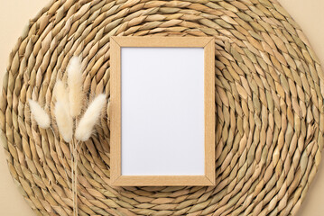 Top view photo of wooden photo frame and branch of white lagurus flowers on decorative placemat with blank space