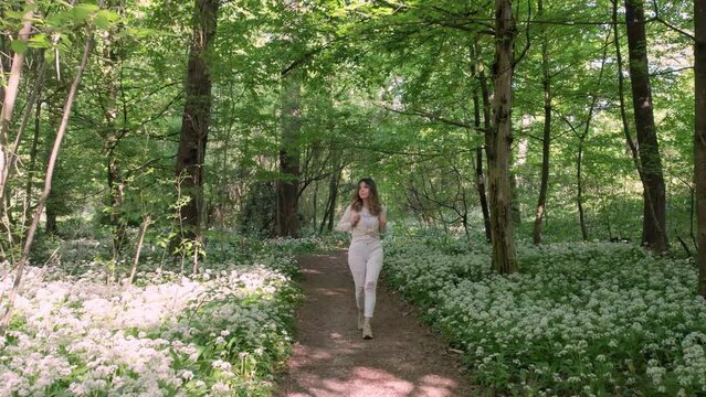 Girl walks in a flowery woods towards camera.