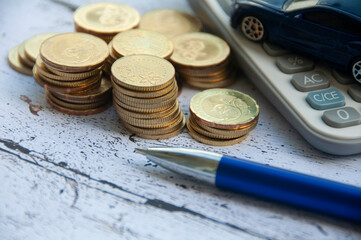 Gold coins, calculator, blue car toy and pen on wooden background. Selective focus on coins.